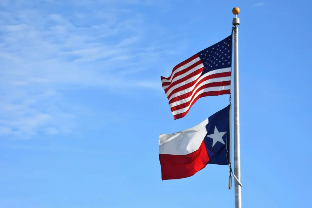 US flag flying above a TX flag against bright blue sky